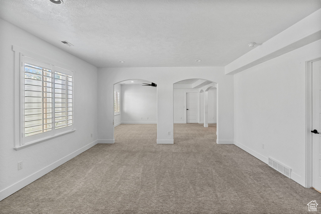 Spare room with arched walkways, carpet flooring, a textured ceiling, and visible vents