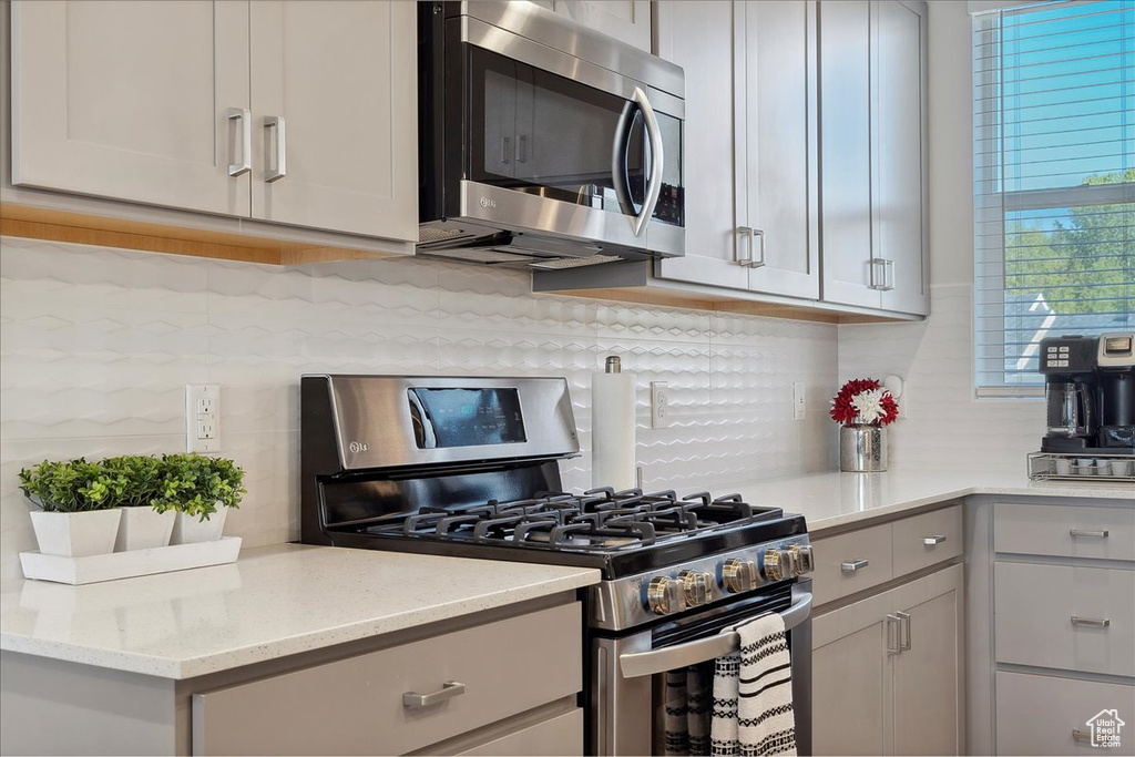 Kitchen featuring light stone counters, tasteful backsplash, gray cabinetry, and stainless steel appliances