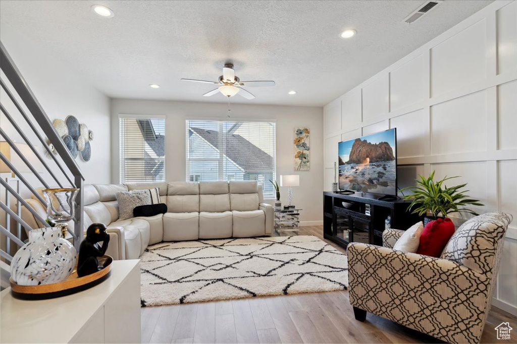Living room featuring a ceiling fan, a textured ceiling, stairs, wood finished floors, and recessed lighting