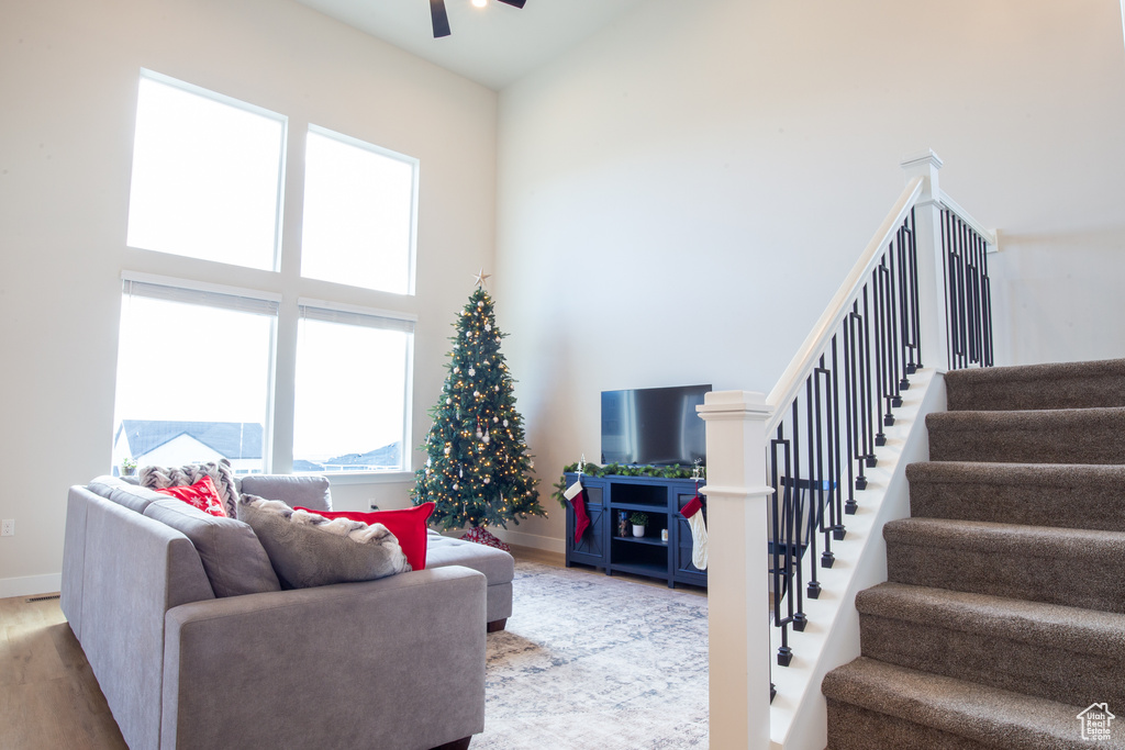 Living area with a towering ceiling, wood finished floors, baseboards, stairway, and a ceiling fan