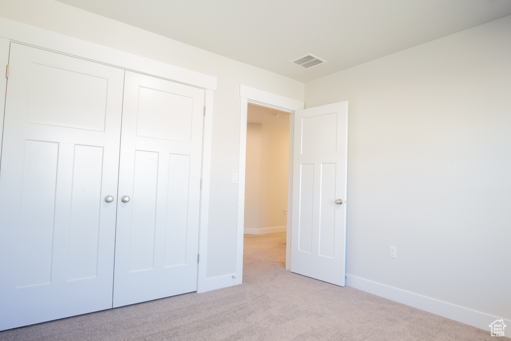 Unfurnished bedroom featuring baseboards, visible vents, a closet, and light colored carpet