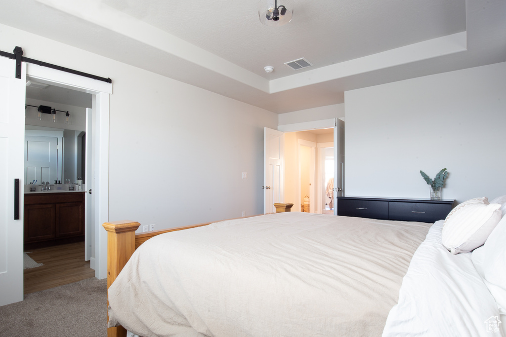 Bedroom with visible vents, a barn door, ensuite bathroom, a tray ceiling, and carpet flooring