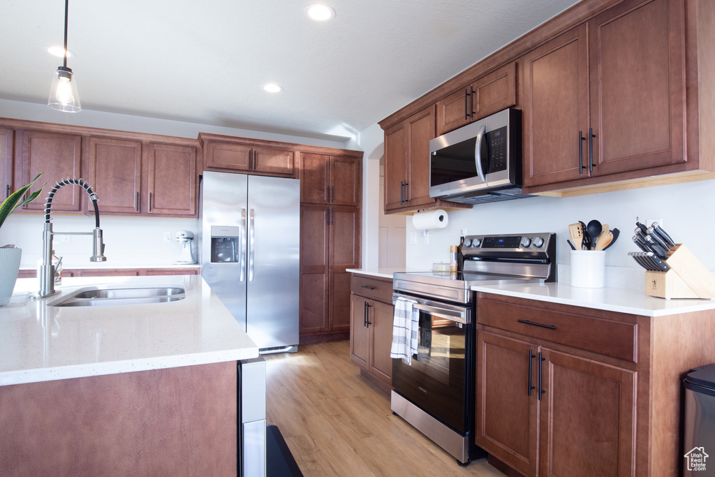 Kitchen with recessed lighting, a sink, light wood finished floors, appliances with stainless steel finishes, and hanging light fixtures