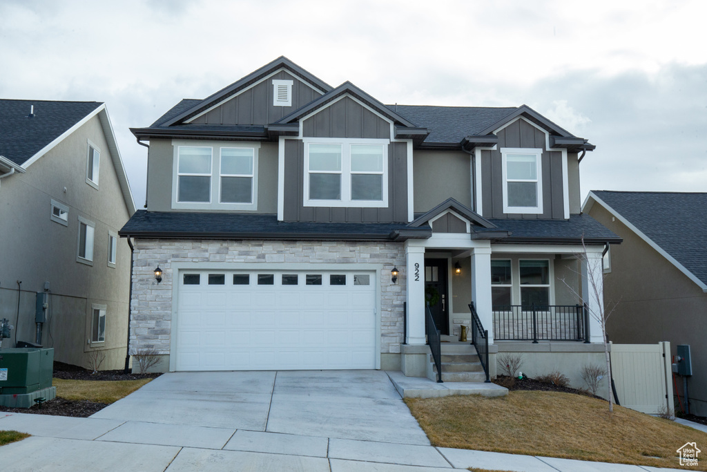 Craftsman-style home featuring stone siding, a garage, board and batten siding, covered porch, and driveway