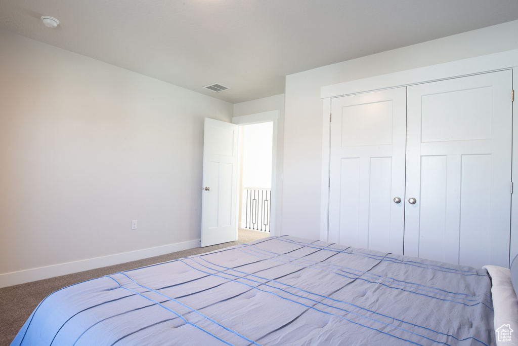 Carpeted bedroom featuring baseboards, visible vents, and a closet