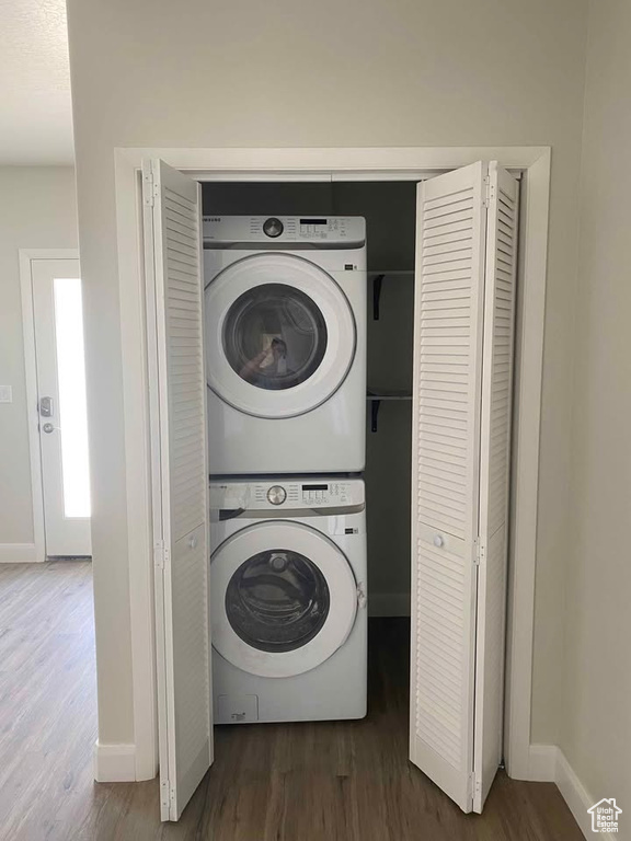 Laundry room featuring laundry area, baseboards, stacked washing maching and dryer, and wood finished floors