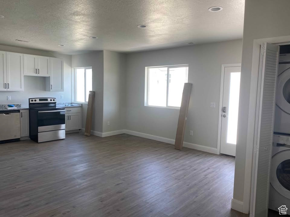 Kitchen featuring stacked washer and clothes dryer, dark wood-style floors, a textured ceiling, white cabinetry, and stainless steel appliances