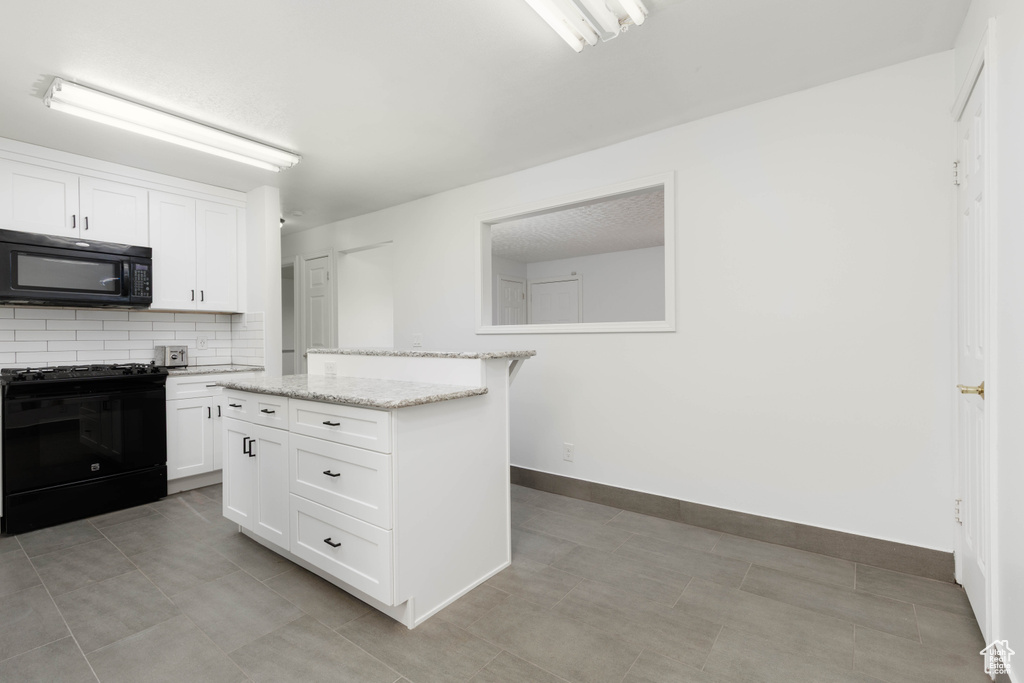 Kitchen featuring light stone countertops, baseboards, white cabinets, backsplash, and black appliances