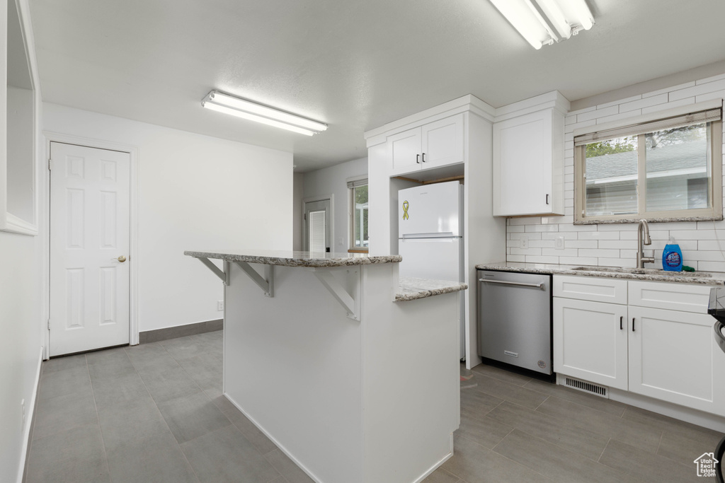 Kitchen featuring visible vents, a center island, stainless steel dishwasher, a sink, and white cabinetry