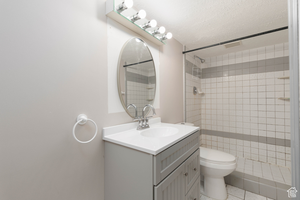Full bathroom with vanity, a textured ceiling, tiled shower, and visible vents