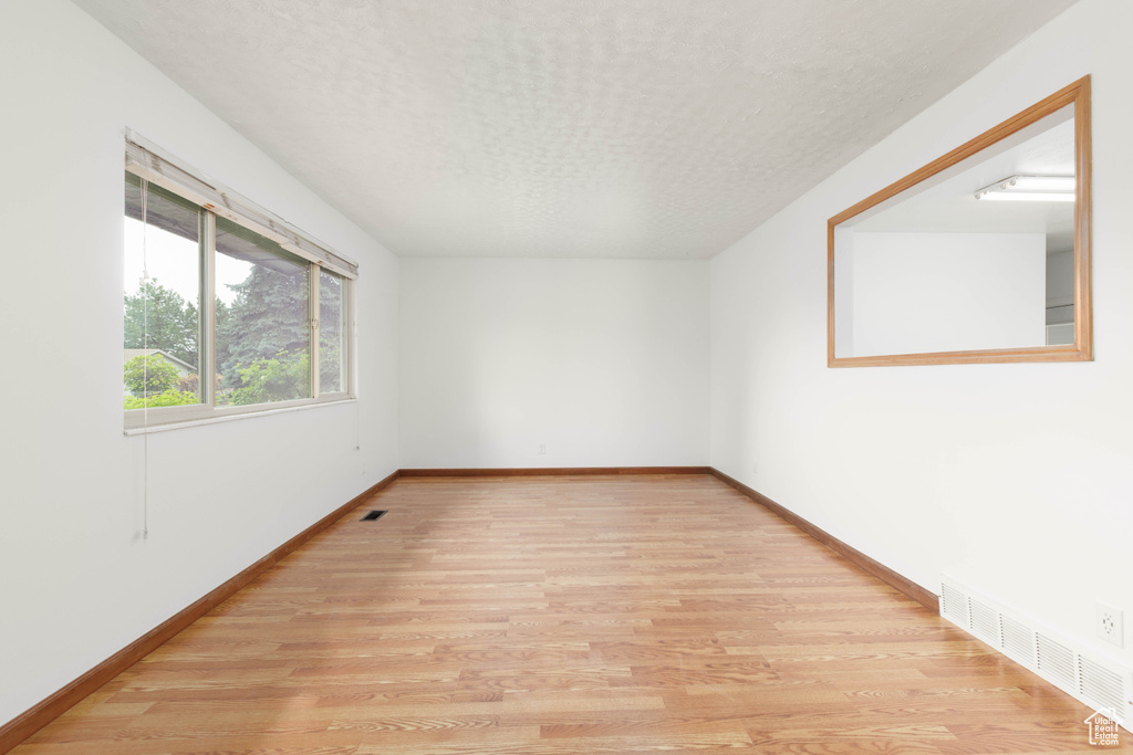 Unfurnished room featuring baseboards, light wood finished floors, a textured ceiling, and visible vents