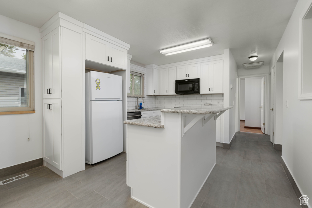 Kitchen with backsplash, visible vents, black microwave, white cabinets, and freestanding refrigerator