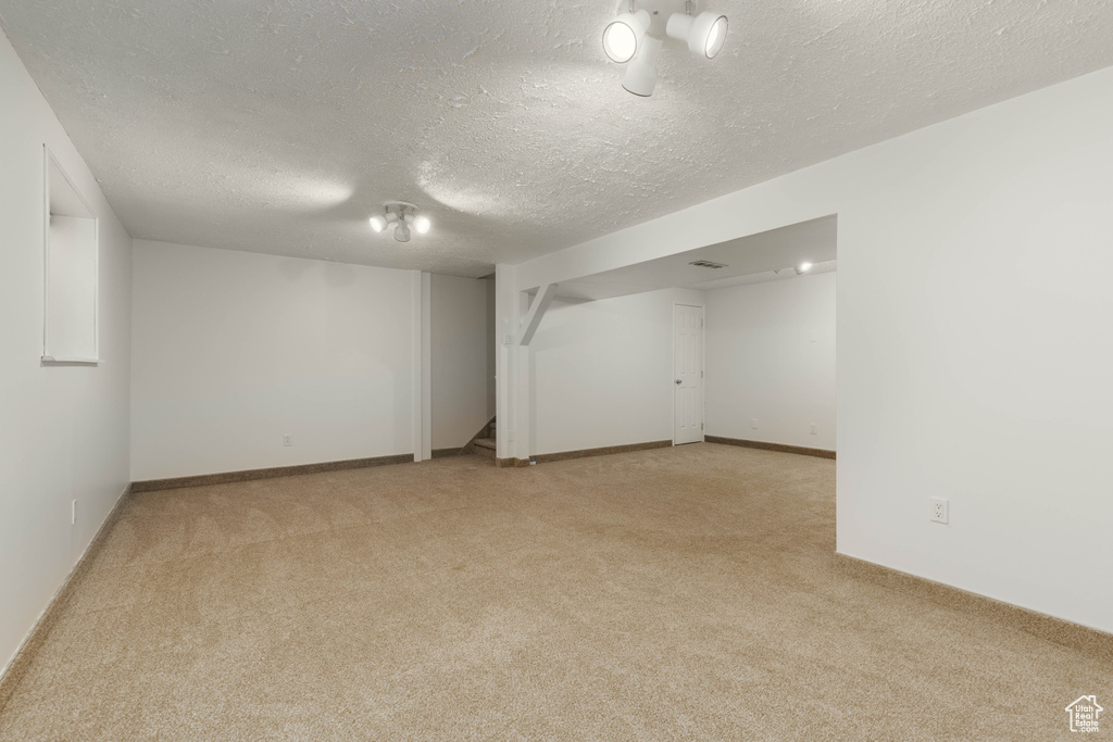 Finished below grade area with baseboards, a textured ceiling, and light colored carpet
