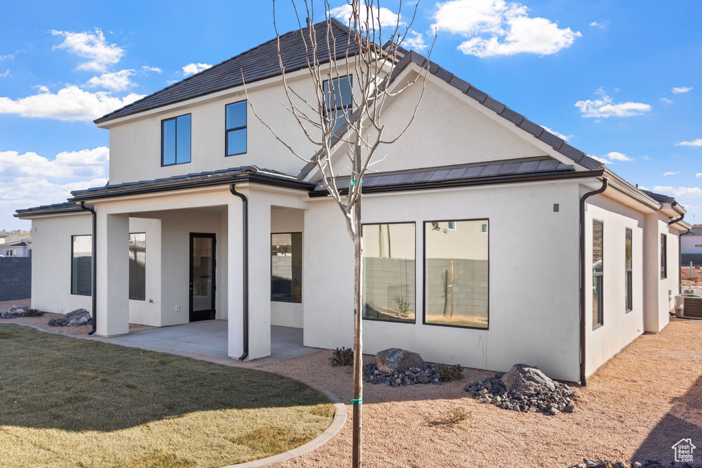 Back of property with a standing seam roof, cooling unit, a yard, a patio, and stucco siding
