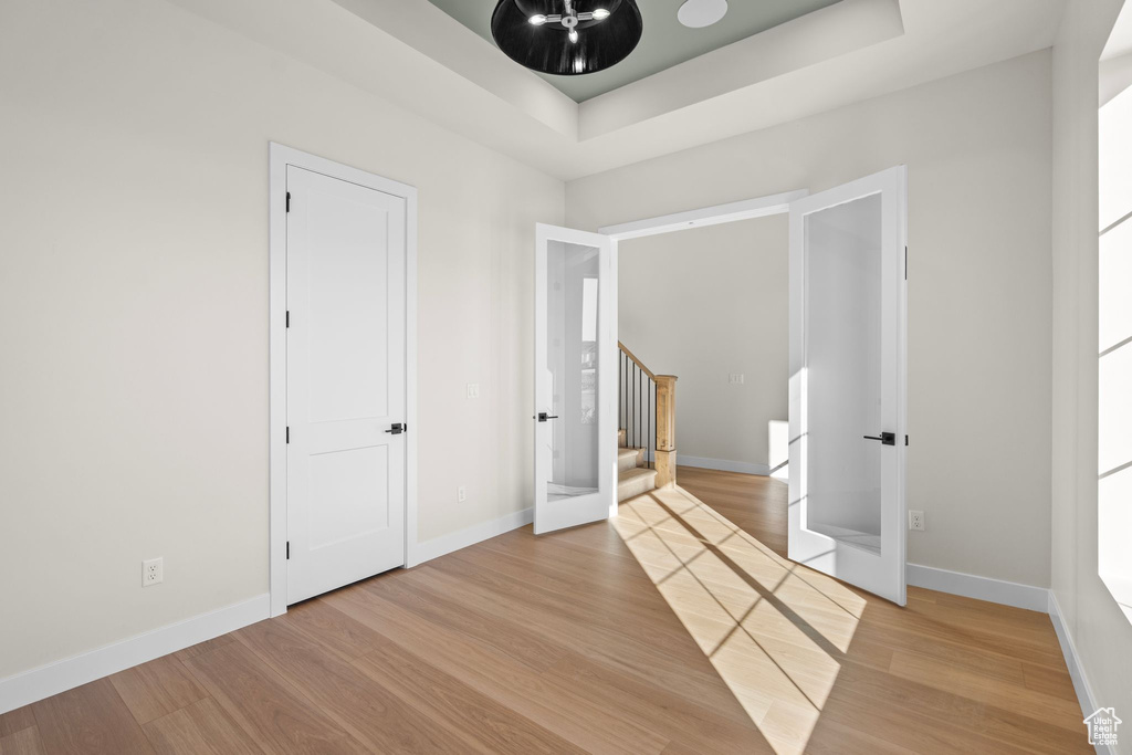Unfurnished bedroom with baseboards, french doors, wood finished floors, and a raised ceiling