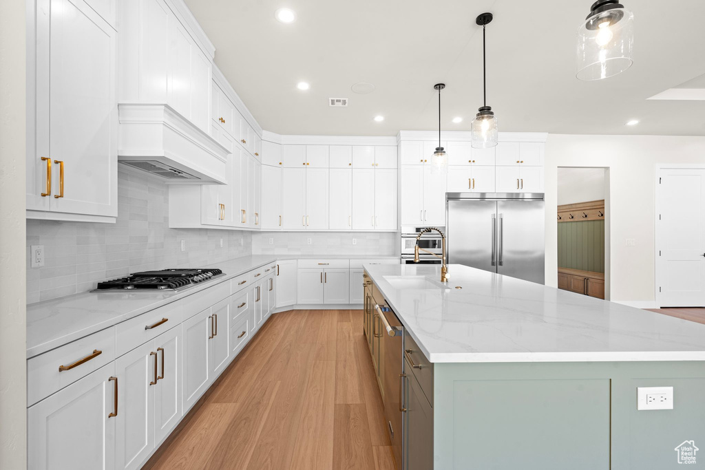 Kitchen featuring appliances with stainless steel finishes, a spacious island, a sink, light wood-style floors, and white cabinetry