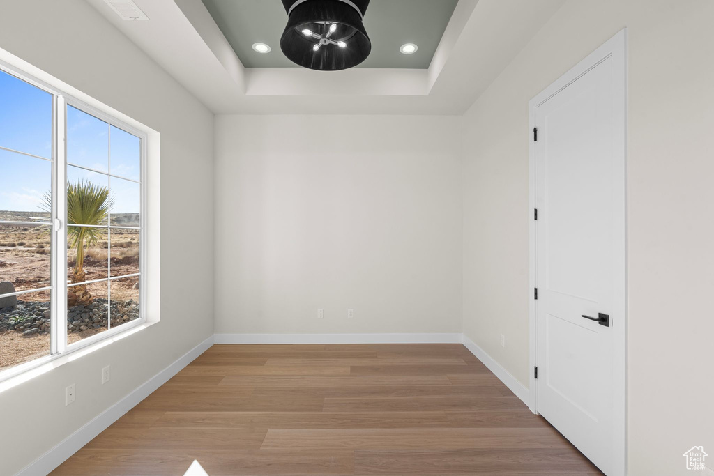 Empty room featuring recessed lighting, baseboards, a tray ceiling, and light wood-type flooring
