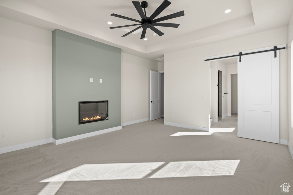 Unfurnished living room featuring a glass covered fireplace, a raised ceiling, recessed lighting, and a barn door