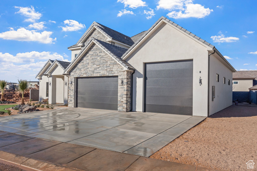 View of front of house featuring an attached garage, stucco siding, stone siding, and concrete driveway