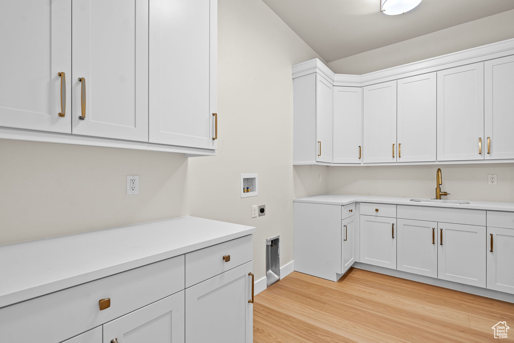 Clothes washing area featuring washer hookup, hookup for an electric dryer, cabinet space, a sink, and light wood finished floors