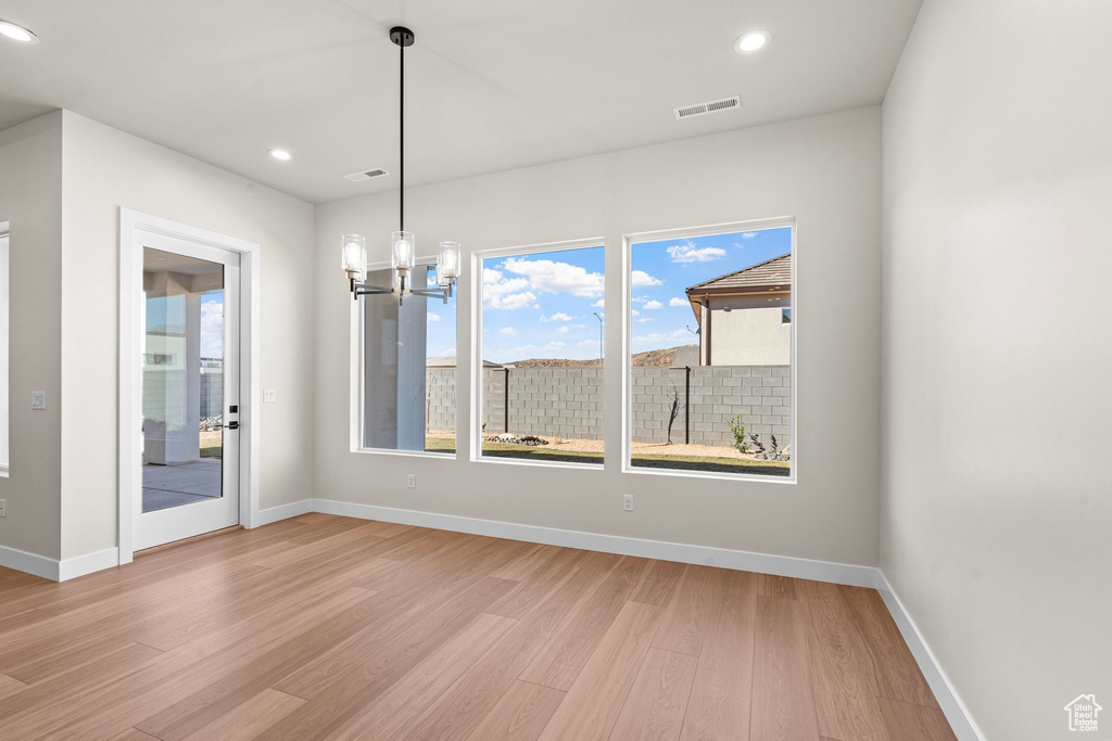 Unfurnished dining area with visible vents, light wood finished floors, baseboards, and a notable chandelier