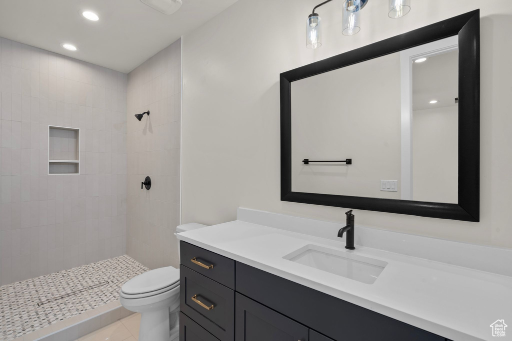 Bathroom featuring a tile shower, tile patterned flooring, vanity, toilet, and recessed lighting