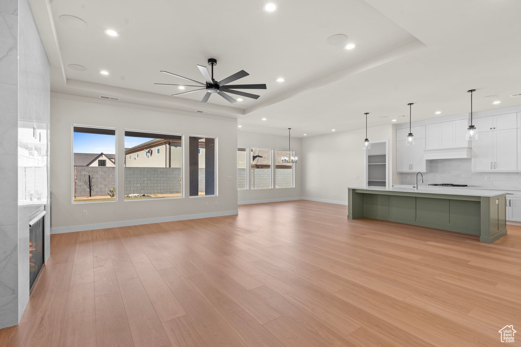 Unfurnished living room featuring baseboards, plenty of natural light, a ceiling fan, and a tray ceiling