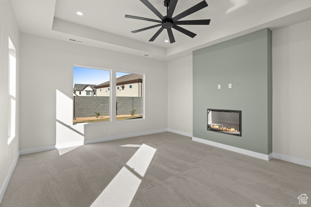 Unfurnished living room featuring visible vents, a raised ceiling, carpet, and a glass covered fireplace