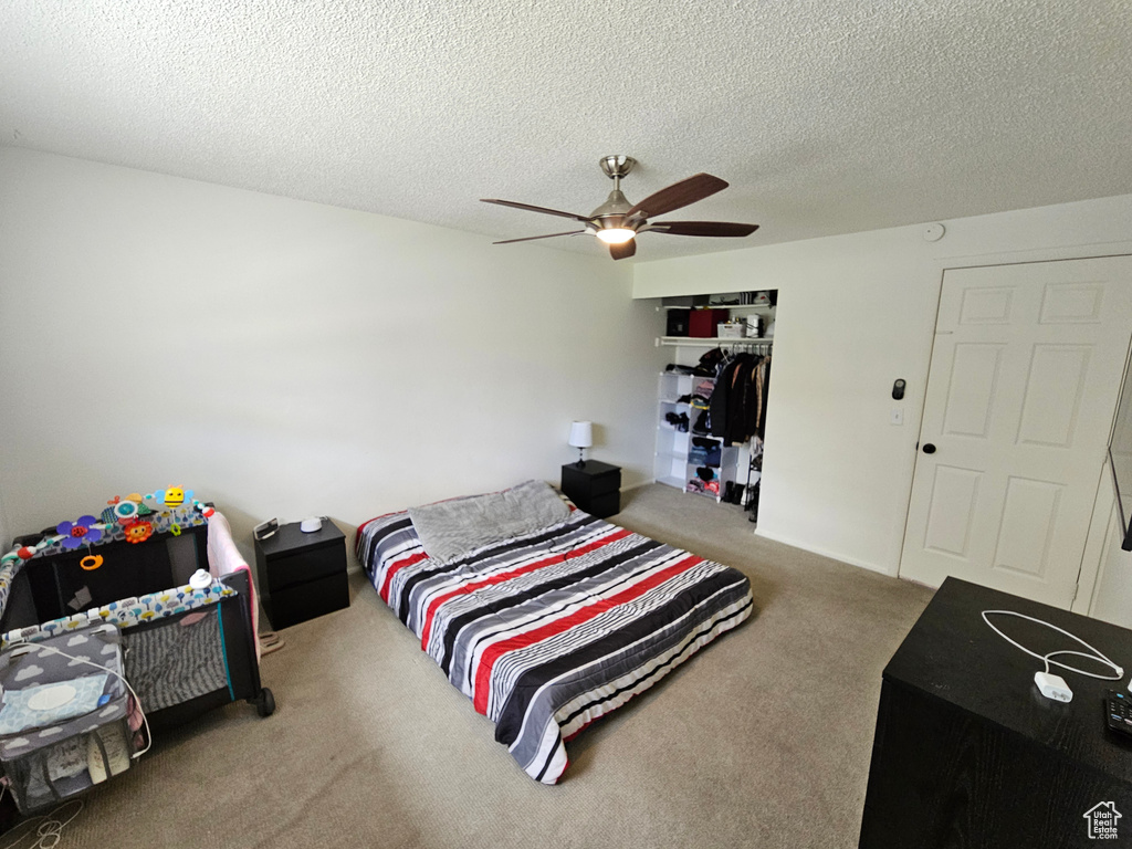 Carpeted bedroom with a ceiling fan, a textured ceiling, and a closet