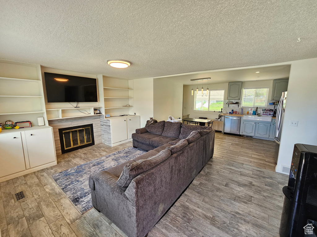 Living room with visible vents, a textured ceiling, light wood finished floors, and a glass covered fireplace
