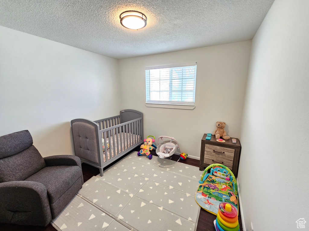 Bedroom with a crib, baseboards, and a textured ceiling