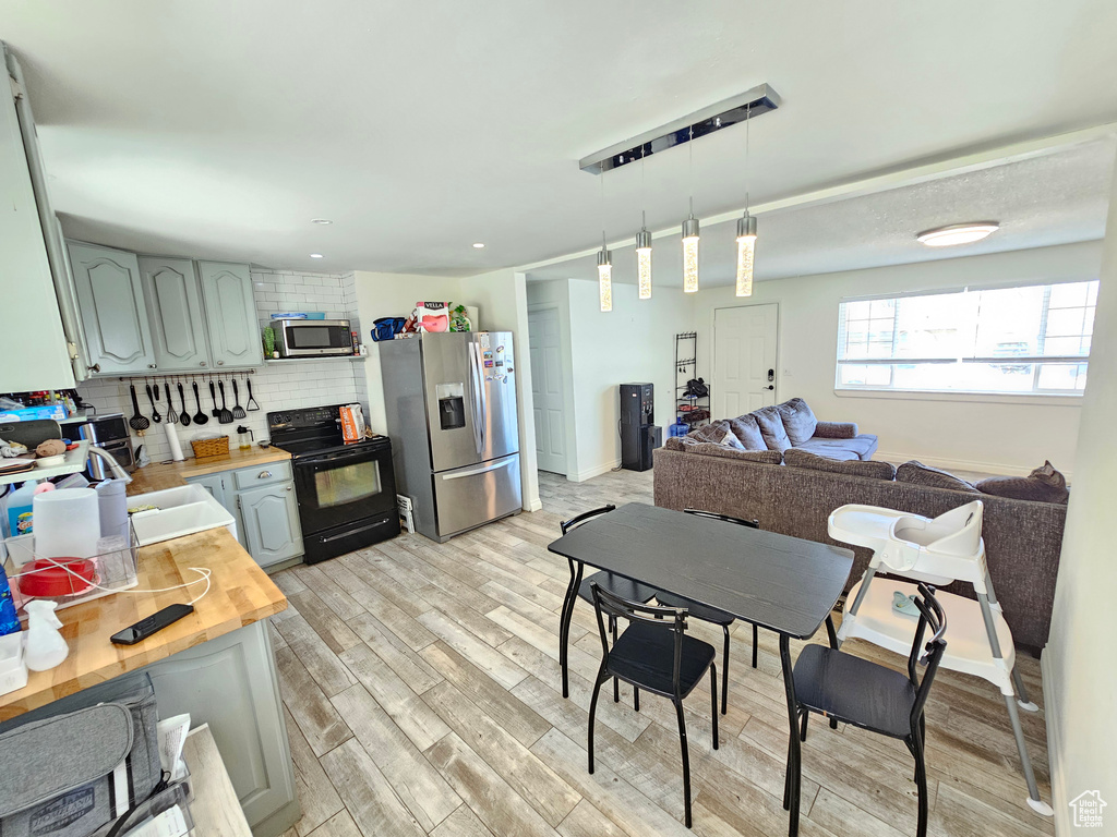 Kitchen featuring decorative backsplash, wooden counters, pendant lighting, appliances with stainless steel finishes, and light wood finished floors