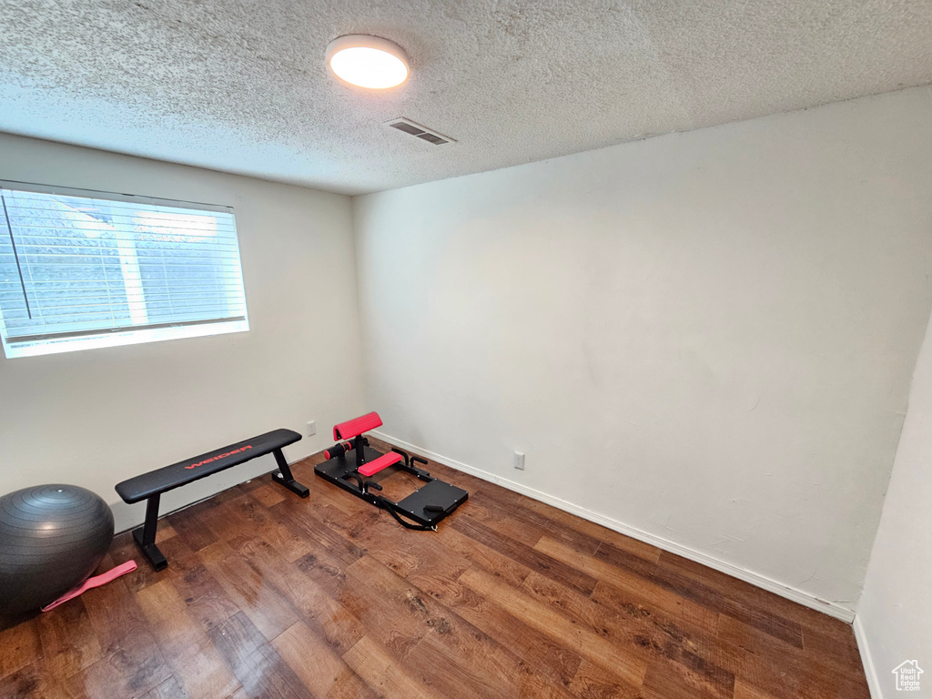 Exercise room with visible vents, baseboards, a textured ceiling, and wood finished floors