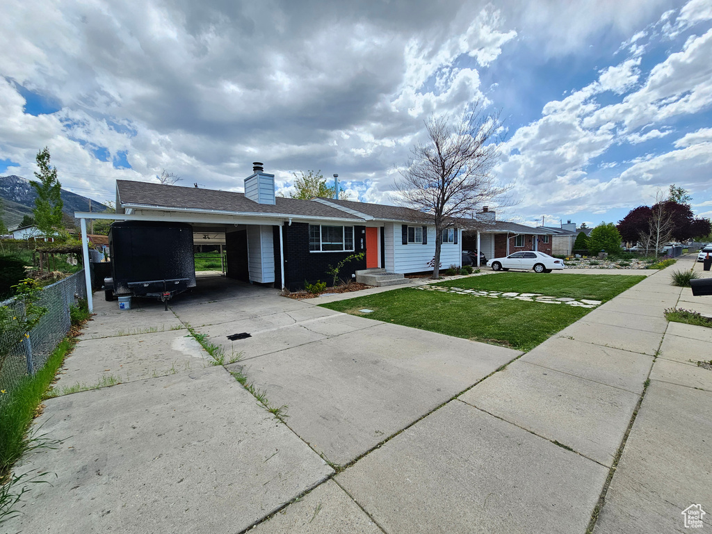Ranch-style house with a front lawn, fence, a chimney, driveway, and a carport
