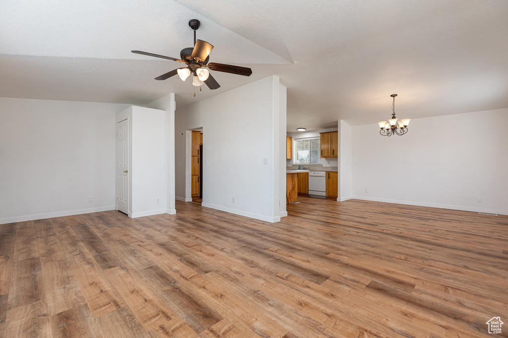 Unfurnished living room with baseboards, ceiling fan with notable chandelier, and light wood-type flooring