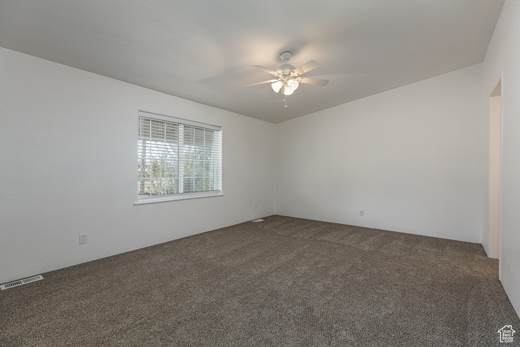 Spare room with ceiling fan, dark carpet, and visible vents