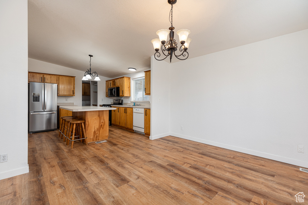 Kitchen with appliances with stainless steel finishes, a center island, wood finished floors, light countertops, and a notable chandelier