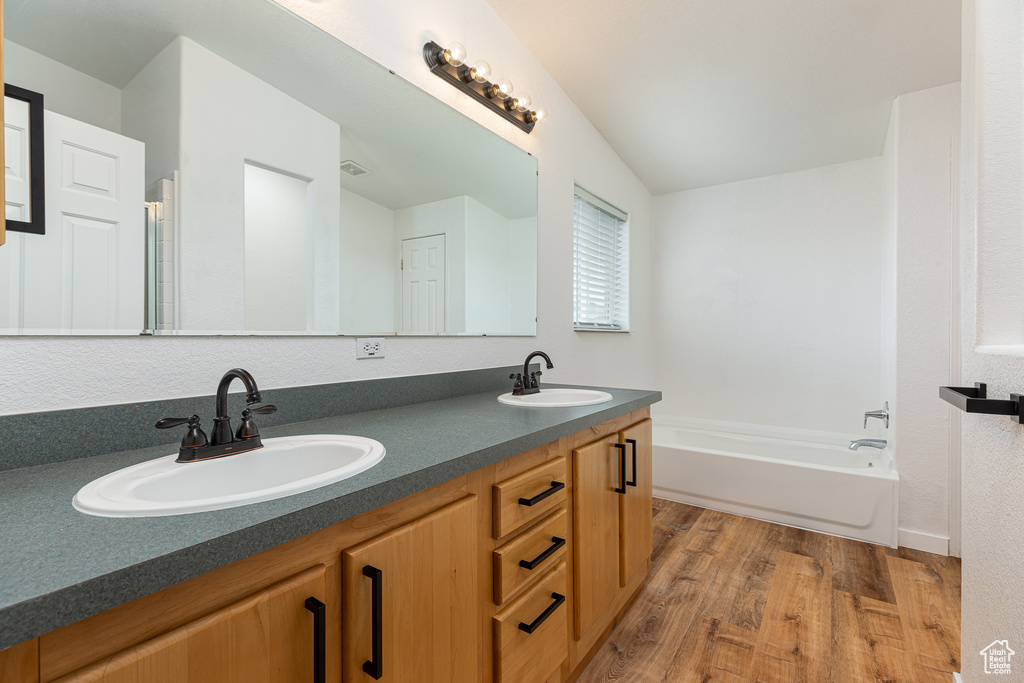 Bathroom with double vanity, a sink, a bath, and wood finished floors