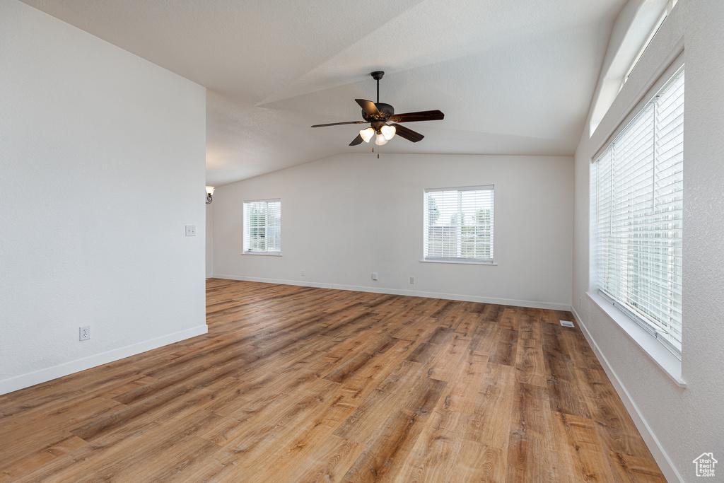 Empty room with baseboards, a ceiling fan, light wood-style flooring, and lofted ceiling