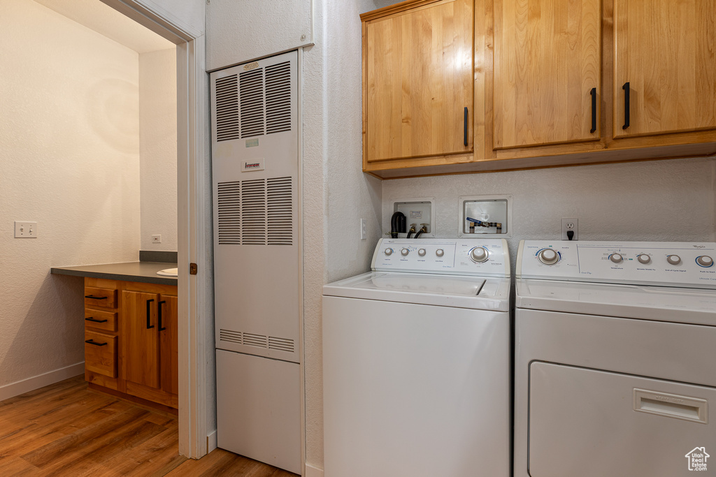 Clothes washing area with washing machine and clothes dryer, light wood finished floors, cabinet space, and a heating unit