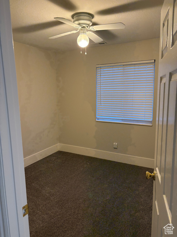 Spare room with a ceiling fan, a textured ceiling, baseboards, and dark colored carpet