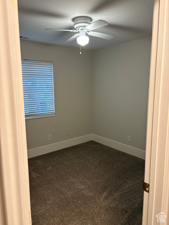 Spare room with baseboards, ceiling fan, dark colored carpet, and visible vents