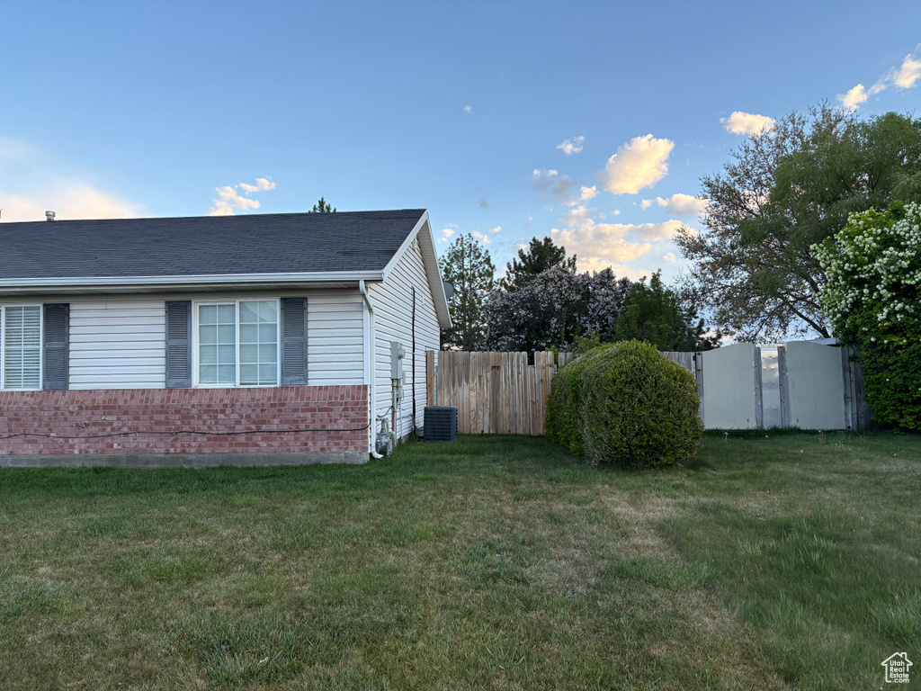 View of side of home with a lawn, brick siding, and fence