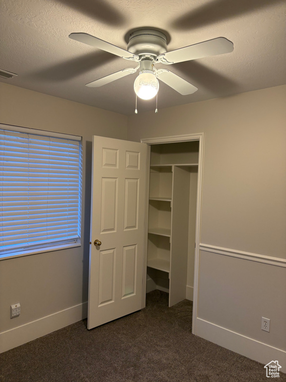 Unfurnished bedroom featuring dark colored carpet, baseboards, ceiling fan, and visible vents