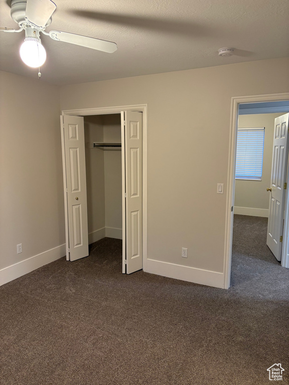 Unfurnished bedroom with a closet, baseboards, ceiling fan, and dark colored carpet