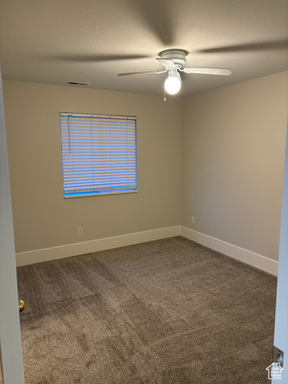Spare room with visible vents, baseboards, ceiling fan, and dark colored carpet