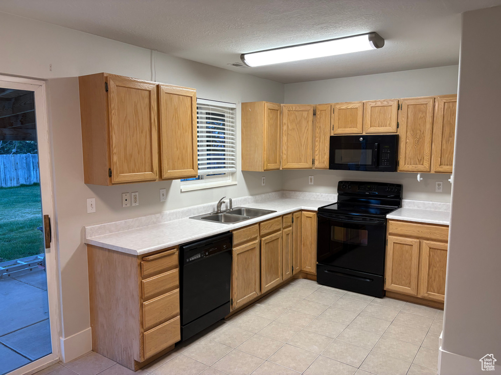 Kitchen featuring light countertops, light tile patterned floors, a sink, and black appliances