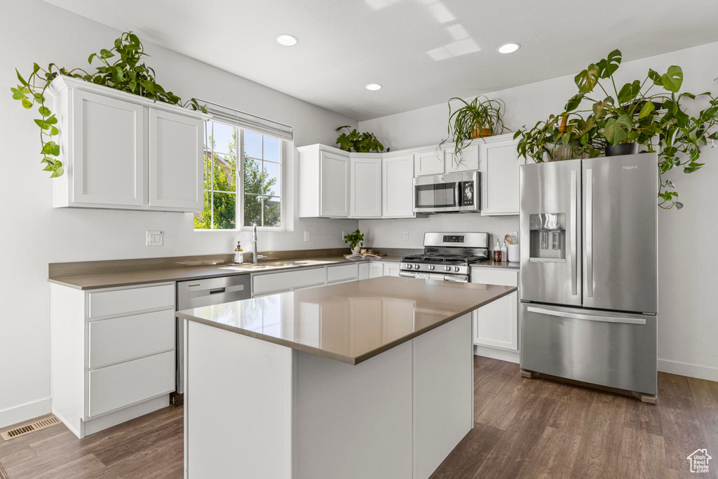 Kitchen featuring dark wood-style floors, a center island, white cabinets, a sink, and stainless steel appliances