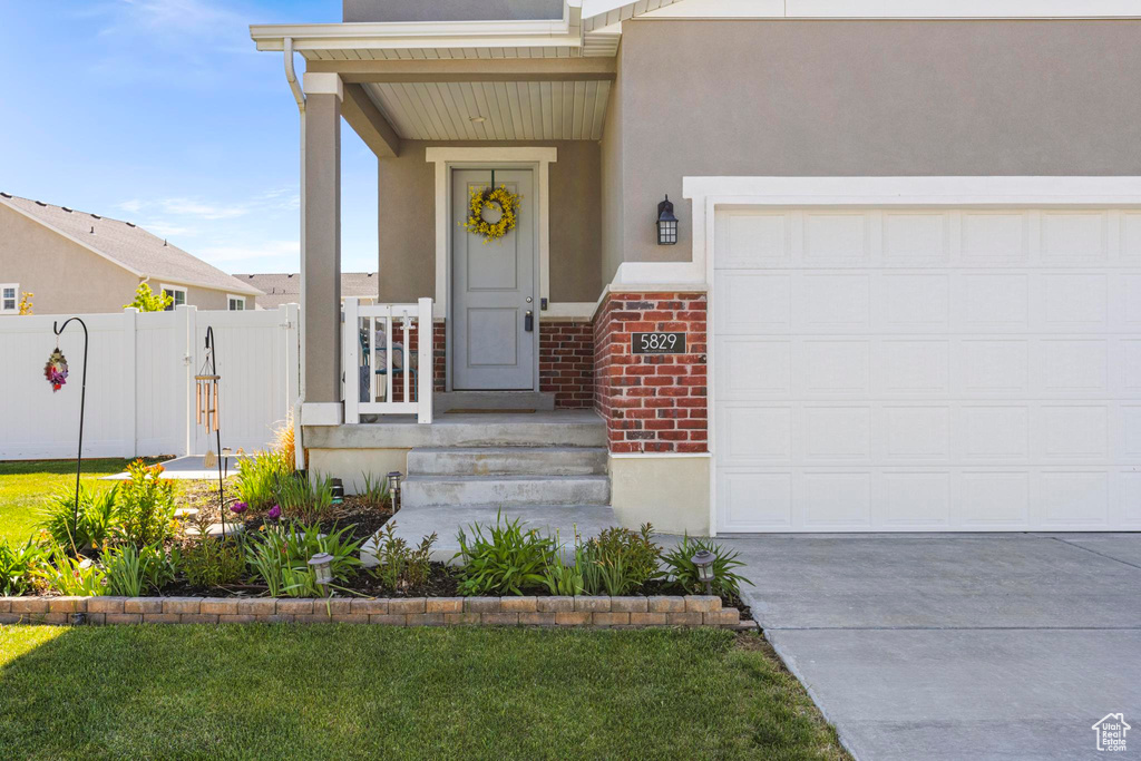 View of exterior entry with an attached garage, stucco siding, driveway, and fence