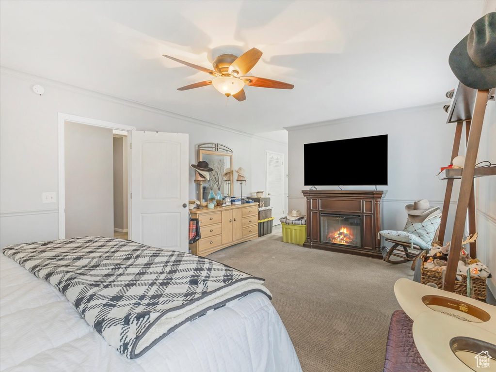 Bedroom with crown molding, ceiling fan, light colored carpet, and a glass covered fireplace